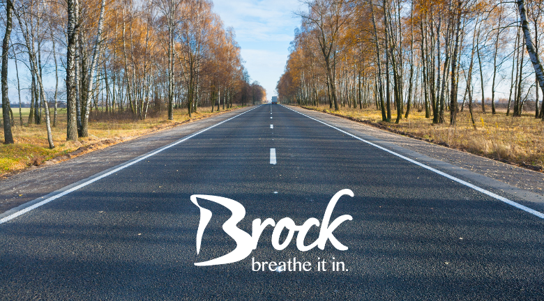 trees lining a paved road. brock logo